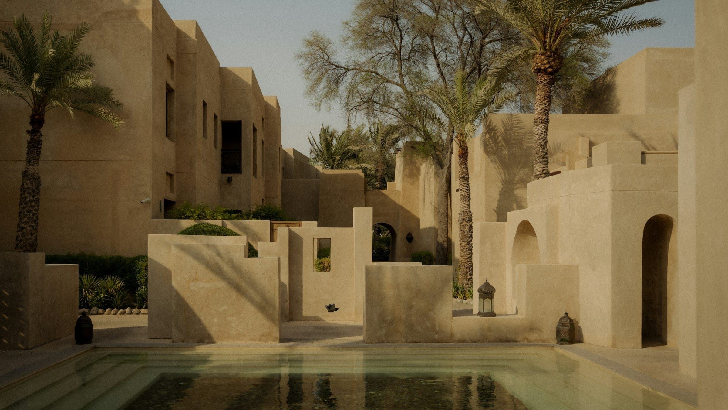 A desert resort courtyard with a pool and palm trees at golden hour