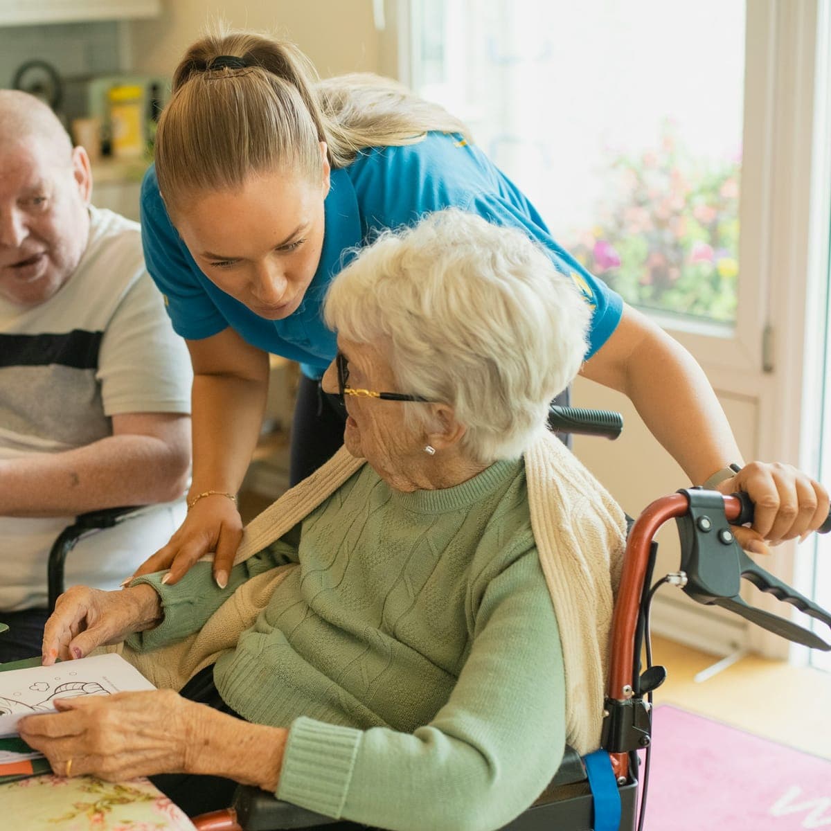A carer joins an older couple for a colouring activity